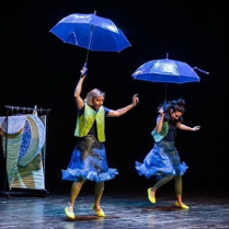 Dwie kobiety na scenie, każda z nich trzyma nad głową granatowy parasol.