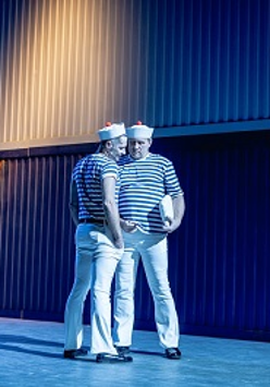 Na scenie dwóch mężczyzn stojących blisko siebie, w strojach przypominających marynarskie. Zdjęcie w niebiesko-błękitnych kolorach.