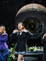 Trzy uśmiechające się kobiety stoją na tle zdjęcia wielkiej gałki ocznej.