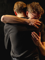 Dwóch mężczyzn przytulających się do siebie, ciemne tło.