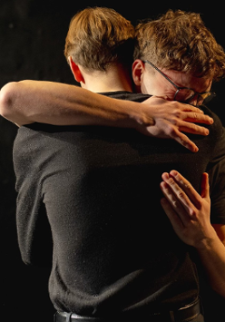 Dwóch mężczyzn przytulających się do siebie, ciemne tło.