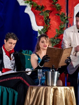 Przy stoliku siedzą kobieta i mężczyzna, oboje trzymają menu. Obok nich stoi kelner, który czeka na zamówienie.