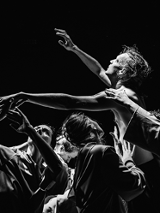 Czarno-białe zdjęcie mężczyzny z uniesionymi rękoma, który podtrzymywany jest przez kilka osób.