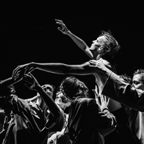 Czarno-białe zdjęcie mężczyzny z uniesionymi rękoma, który podtrzymywany jest przez kilka osób.