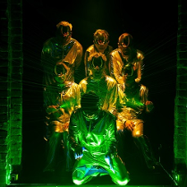 Kilka osób w skafandrach i maskach oświetlonych zielono-żółtym światłem.