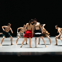 Scena ze spektaklu - tancerze na scenie, w środku dwie tancerki blisko siebie, dotykają się głowami.