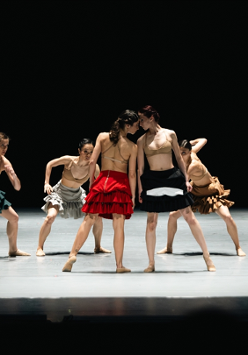 Scena ze spektaklu - tancerze na scenie, w środku dwie tancerki blisko siebie, dotykają się głowami.