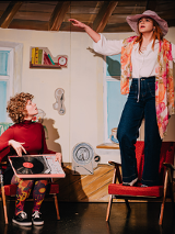 Dwie młode dziewczyny, jedna siedzi i trzyma na kolanach płyę winylową, druga stoi z rozłożonymi rękoma na fotelu.