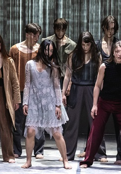 Grupa tancerzy w różnorodnych strojach, wszyscy stoją z opuszczonymi głowami.