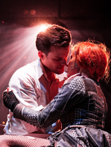 Zdjęcie obejmujących się kobiety i mężczyzny, ich twarze są blisko siebie. Z tyłu pada na nich rozproszone światło.