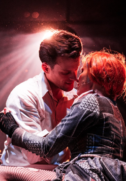 Zdjęcie obejmujących się kobiety i mężczyzny, ich twarze są blisko siebie. Z tyłu pada na nich rozproszone światło.