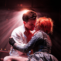 Zdjęcie obejmujących się kobiety i mężczyzny, ich twarze są blisko siebie. Z tyłu pada na nich rozproszone światło.