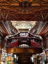 Wnętrze biblioteki wypełnionej książkami na drewnianych regałach. W centrum widoczne są schody.