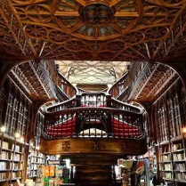 Wnętrze biblioteki wypełnionej książkami na drewnianych regałach. W centrum widoczne są schody.