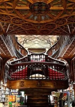 Wnętrze biblioteki wypełnionej książkami na drewnianych regałach. W centrum widoczne są schody.