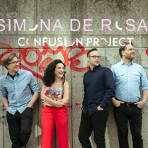 Czworo osób stoi przy betonowej ścianie pokrytej czerwonym graffiti. Trzech mężczyzn i jedna kobieta uśmiechają się i patrzą w jedną stronę. Na górze obrazu widnieje napis w różowo-białym kolorze: "Simona De Rosa, Confusion Project".