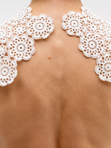 Artystyczne ujęcie przedstawiające nagie plecy i ramiona osoby, na których ułożona jest biała, koronkowa serweta wykonana z połączonych okrągłych elementów o kwiatowym wzorze. Zdjęcie wykonane na jednolitym białym tle.