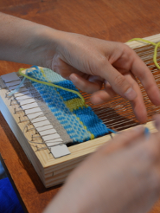 Dłonie wyplatające kolorową tkaninę na ręcznym, prostym krośnie.