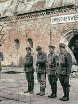 Grupa rekonstruktorów armii pruskiej stoi szeregiem przed ceglanym wejściem do fortu.