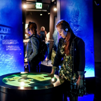A girl with headphones on looks at the illuminated tabletop with documents displayed on it. Photo in blue colors.