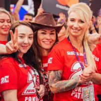 A group of girls in red t-shirts of the WOŚP information service smile at the camera.