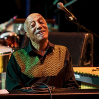 A photo of a smiling musician with musical instruments behind him.