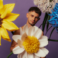 A young man standing behind and among big flowers.