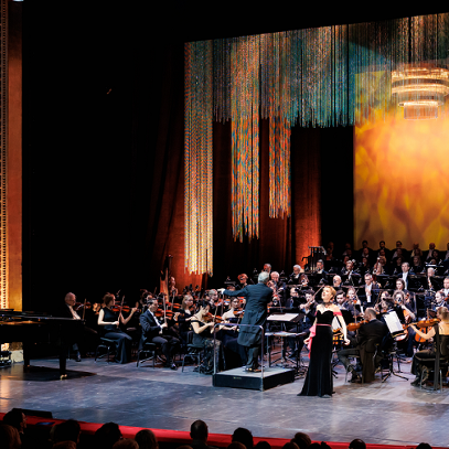 An opera singer performing on stage, with an orchestra behind her.