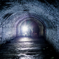 An underground corridor, at the end of which there are several people with flashlights.