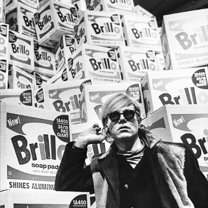 Black and white photo of a person in front of boxes of soap pads. The person is holding their hand to his or her ear.