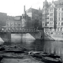 Black and white photo of the river, a few boats, the bridge and buildings along the river.