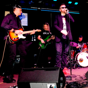 Photo of the band performing on stage - one man is singing, two men are playing the guitar.