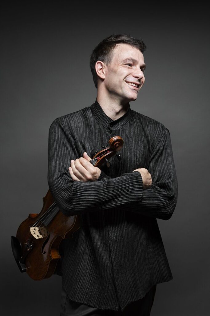 Photo of the artist, Amihai GROSZ, who is holding the violin in his hand