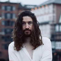 Photo of the singer - young, long-haired man in white shirt.