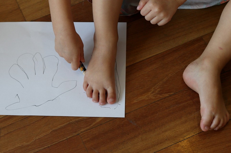 Photo of a child's feet and one hand, which is drawing a line around one foot on a piece of paper.