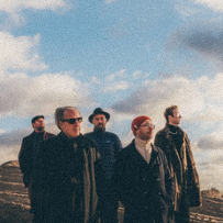 Five men standing on the field, blue sky and white clouds as a background.