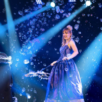 Photo from the performance - a woman in long, blue dress on stage blowing bubbles.