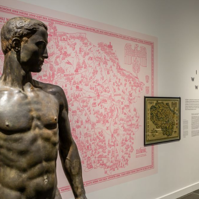 In the foreground there is a sculpture of a naked man, in the background on the wall there is, among other things, a pink city map.