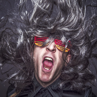 Photo of a man's face with open mouth, colourful glasses and curly hair.