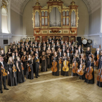 Orchestra musicians pose with their instruments in front of the organ in the Adam Mickiewicz University Auditorium.