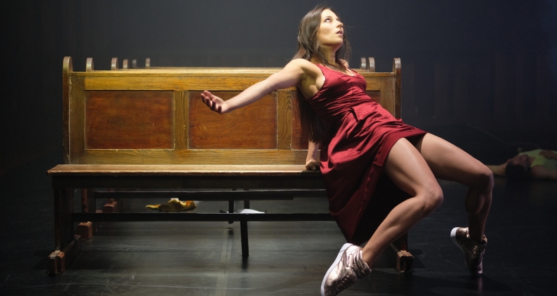 Picture of a dancer in a red dress and white sneakers on a wooden bench
