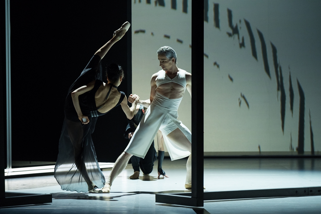 Two ballet dancers - a woman in black dress and a man in white garment in dance poses.