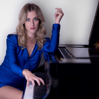 Photo of Francesca Tandoi in a blue dress, sitting at the piano.