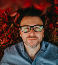 Photo of the artist - man in glasses in blue shirt on red background