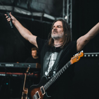 Photo of Ray Wilson on stage - he stands with his arms raised up, holding a microphone in one hand.