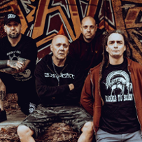 Photo of The Exploited band - four men in dark clothes; wall with graffiti as a background.