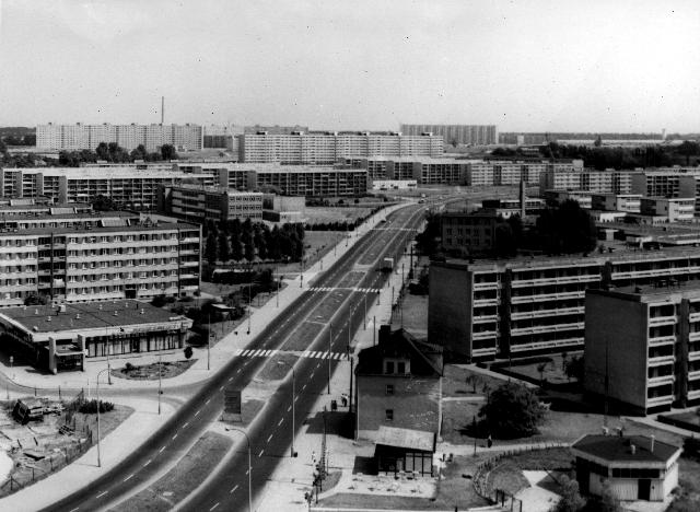 A black and white photograph of a bird's eye view of a landscape with apartment blocks and a two-lane road running diagonally