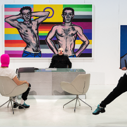 Photo of two men, one sitting at the desk, another opposite him in an arm-chair. Colourful picture on the wall as a background.