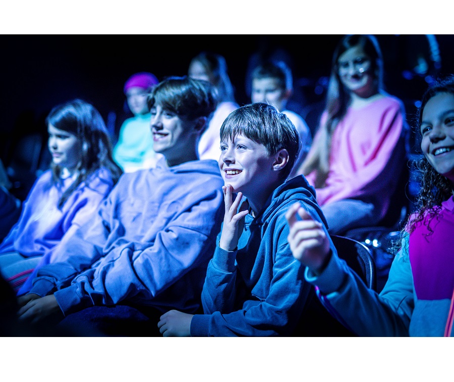 Na zdjęciu nastolatki siedzące w kinie, patrzą na ekran, śmieją się.