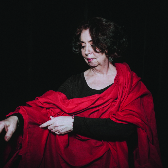 Kobieta w czarno-czerwonym stroju stoi na ciemnym tle.